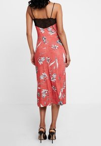 Robe midi à motifs floraux en corail avec un bustier en dentelle noire. Dotée de fines bretelles et d'une silhouette ajustée. Tissu lisse et texturé.
