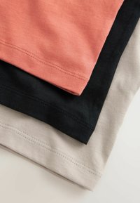 Trois t-shirts empilés : un corail, un noir et un beige. Tous sont en coton avec une texture lisse et des coutures visibles le long des ourlets.