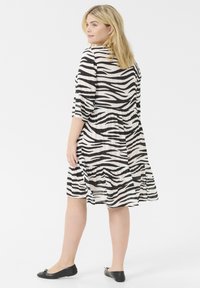 Kleid mit Zebra-Muster in Schwarz und Creme, mit gestuftem Saum, Dreiviertelärmeln und lockerer Passform, kombiniert mit schwarzen Ballerinas.