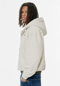 Lys grå hættetrøje med frontlynlås, sidelommer, ribbede manchetter og kant, båret med blå jeans. Enkel, afslappet design.