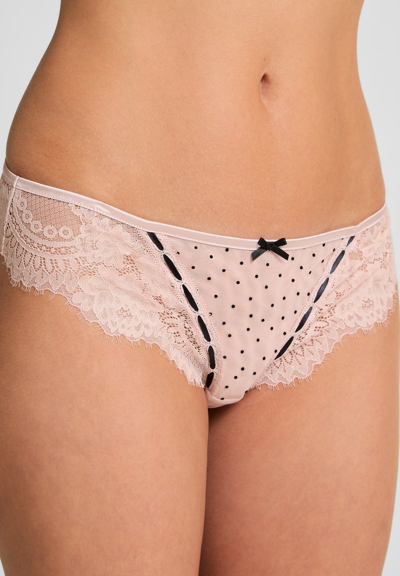 Lichtroze lingerie met zwarte stippen. Voorzien van kantafwerking, geschulpte randen en een klein zwart strikje als accent. Gladde stof en verfijnd ontwerp.