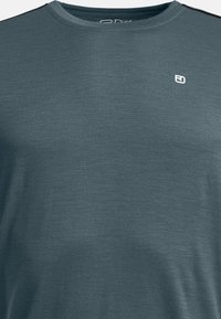 Short-sleeve, round-neck t-shirt in dark teal fabric with a subtle texture. Features a small white logo on the upper left side.