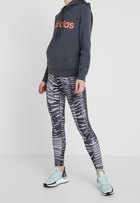 Tmavě šedá mikina s oranžovým logem, doplněná černými a bílými legínami s potiskem. Lehké sportovní boty s aqua akcenty dotvářejí celý vzhled.