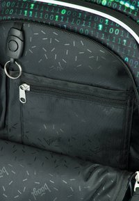 Interno di uno zaino nero con una tasca con zip, caratterizzato da un motivo a codice binario e sottili accenti tratteggiati sul tessuto, texture liscia.
