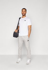 Hvid kortærmet t-shirt med sort logo, grå sweatpants med sorte accenter, og en sort taske. Hvide sportssko fuldender outfittet.