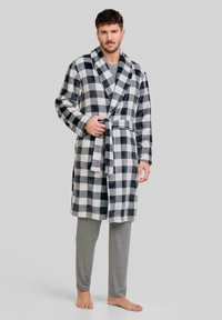 Bata de franela en patrón de cuadros en blanco y negro, con cuello chal, cinturón de lazo y mangas largas, usada sobre pantalones grises.