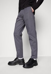 Gray trousers with a relaxed fit, crafted from smooth fabric. Paired with black lace-up shoes featuring a thick sole and contrasting white socks.