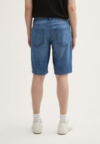 Blauwe denim short met een relaxte pasvorm, opgerolde boorden en twee achterzakken, gecombineerd met witte sneakers en witte crew socks.