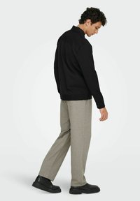 Svart jakke med krage, lett stoff. Kombinert med beige bukser og svarte sko, med avslappet passform og enkel design.