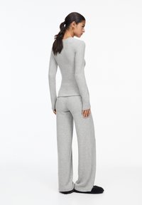 Set di top a maniche lunghe grigio e pantaloni a gamba larga realizzato in tessuto morbido. L'outfit presenta un design semplice con maniche lunghe e una vestibilità aderente.