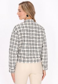 Fekete-fehér kockás tweed zakó, rövid fazonnal, álló gallérral és hosszú ujjal. Texturált anyag, strukturált illeszkedéssel.