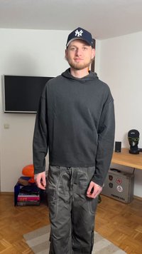 Sort hættetrøje med snøre, løstsiddende design. Olivengrøn cargo-bukser med lommer og snore. Navy baseballkasket med hvidt logo.