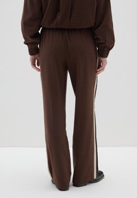 Bruine geruite wijde broek met een elastische tailleband, voorzien van zijstreepaccenten in crème en donkerbruin; zachte stofstructuur.