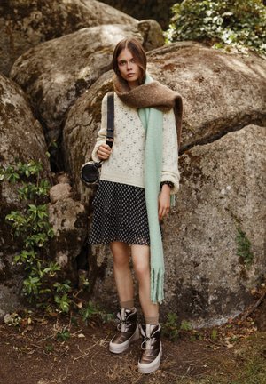 Suéter con un intrincado patrón de punto, color beige claro; falda de lunares; bufanda marrón y verde menta; botas metálicas marrones con suelas gruesas.