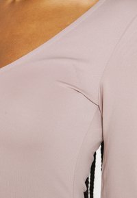 Camisola de manga longa rosa claro com design em V, apresentando uma textura suave e ribateada e detalhes de costura subtis nas costuras.