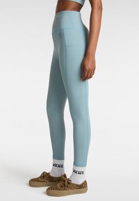 Leggings blu alti in vita con cuciture azzurre a contrasto e tasche laterali, abbinati a scarpe con stampa leopardata e calzini bianchi.