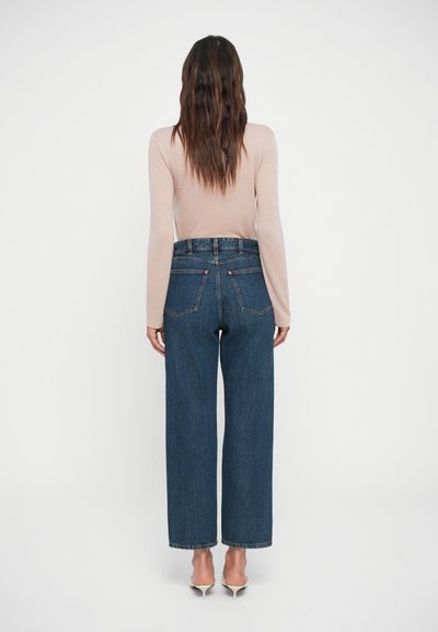 Jeans de mezclilla de tiro alto y pierna ancha en azul oscuro. Cuenta con bolsillos traseros y un corte recto. Combinado con una blusa ajustada de manga larga.