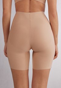 Nude hoge taille shorts gemaakt van glad, rekbaar materiaal, met een snit tot halverwege de dij en minimale naden voor een naadloze uitstraling.
