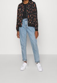 Černá bomber bunda s oranžovým a bílým cik-cak vzorem, spárovaná s světle modrými džíny s vysokým pasem a bílými teniskami. Ležérní outfit.