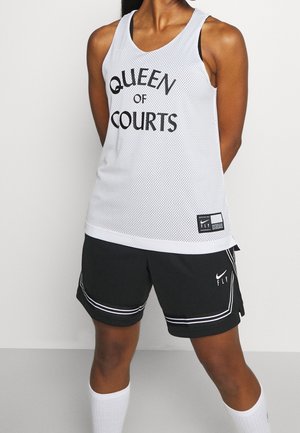 Kobieta ubrana w biały sportowy bezrękawnik z napisem „Queen of Courts”, czarne sportowe spodenki z białymi paskami oraz białe skarpetki sięgające do kolan.