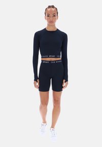 Tengerészkék hosszú ujjú sportfelső hüvelykujjlyukakkal és hozzáillő, magas derekú rövidnadrág. Fehér "TED BAKER SPORT" felirattal a derékpánton.