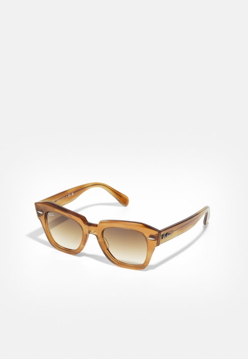 Óculos de sol retangulares com tonalidade âmbar, lentes graduadas, armação grossa e textura suave. Apresenta uma marcação discreta na lateral.