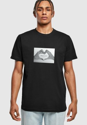 Sort t-shirt i sort bomuld med et centralt grafik af to hænder, der danner en hjerteform, med teksten "alt hvad du behøver er" nedenfor.