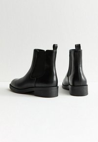 Botas Chelsea de cuero negro con paneles laterales elásticos, un tirador y un tacón bajo apilado. Textura suave con un diseño minimalista.