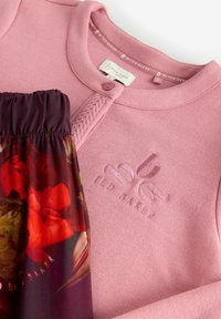 Roze gebreide top met een ronde halslijn en textuurdetails, gecombineerd met plompe bloemenpatroon stof. Heeft een reliëf logo.