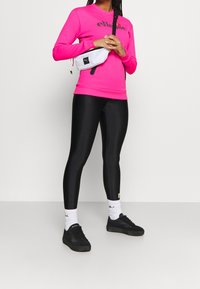 Felpa rosa con logo, leggings neri, marsupio bianco e sneakers nere; include calzini bianchi con logo. Texture lisce in tutto.