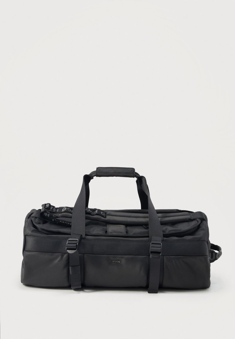 Μαύρη ορθογώνια τσάντα duffel με διπλές λαβές, ρυθμιζόμενους ιμάντες, μπροστινή τσέπη και το λογότυπο "HUGO" σε απλό φόντο.