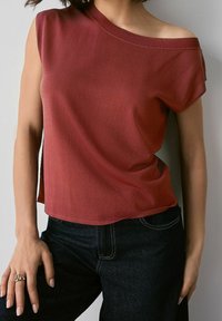 Haut rouge à manches courtes avec un décolleté asymétrique, doté d'une texture douce, associé à un jean en denim foncé. Design simple sans motifs.