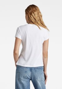 T-shirt en coton blanc avec un col rond et des manches courtes, présentant une coupe décontractée et une texture lisse. Associé à un jean bleu clair.
