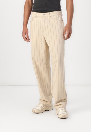 Pantaloni beige con righe blu verticali, dotati di chiusura a bottone e tasche laterali, realizzati in un tessuto morbido e testurizzato.