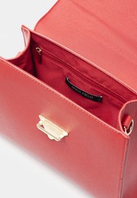 Czerwona torebka skórzana o teksturze z złotym zapięciem, otwarta, aby pokazać czerwony materiał wewnętrzny i kieszeń na zamek.