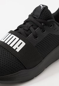 Zwarte sportieve schoen met een bovenwerk van mesh, gevoerd kraagje, elastische band met witte branding en een gestructureerde rubberen zool.
