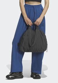 Μαύρη φουσκωτή τσάντα χειρός με διπλές λαβές, που διαθέτει υφή με καπιτονέ επιφάνεια. Συνδυάζεται με φαρδιά μπλε παντελόνια και μαύρα αθλητικά παπούτσια.