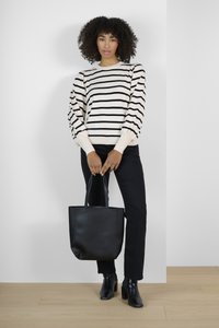 Maglione a righe crema con maniche a palloncino, abbinato a pantaloni neri e stivaletti. Borsa nera tenuta tra le mani, su un pavimento in legno chiaro.