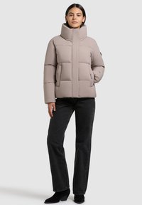 Puffet jakke i lys beige med høj krave, quiltet design, sidelommer og en afslappet pasform, parret med sorte jeans og ankelstøvler.