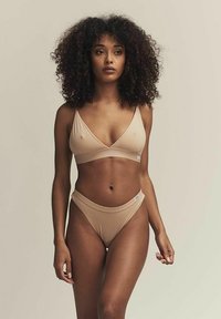 Nude-färgad bikiniuppsättning som består av en v-ringad bralette med justerbara axelband och höga baddräktsbottoms, tillverkad av mjukt tyg.