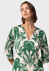 Blusa a maniche corte color crema con motivi a foglia verde, con una scollatura a V profonda e tessuto leggero e morbido.