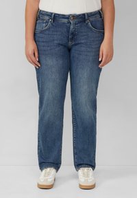 Niebieskie dżinsy typu skinny z prostą nogawką, pięcioma kieszeniami i subtelnym przetarciem. W połączeniu z białymi sneakersami.