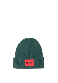 Bonnet en tricot vert avec une texture côtelée, présentant une patch rectangulaire rouge avec du texte noir. Design classique à revers.