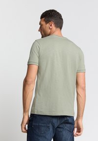 Lichtgroen kortmouwen shirt met een ronde hals, gemaakt van zachte stof. Draag het met donkerblauwe jeans, die een gladde textuur en een ontspannen pasvorm tonen.