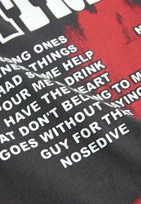 T-shirt avec texte blanc sur fond noir et rouge comportant des mots partiels tels que « SOME HELP », « DRINK », « HEART » et « NOSEDIVE ».