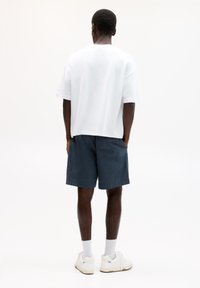 Weißes Baumwoll-T-Shirt mit lockerer Passform, maritime Shorts und weißen Sneakern. Strukturiertes Material und ein lockeres Design.