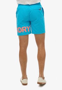 Bermudas de baño azules con "DRY" en grandes letras rosas, con una cinturilla elástica, un bolsillo trasero y una textura smooth.