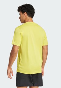 Short-sleeve t-shirt in bright yellow fabric, featuring a simple design and smooth texture, worn with black shorts, showing the back view.