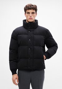 Jachetă puffer neagră cu guler înalt, dotată cu închidere cu butoane și manșete cu textură ribbon. Materialul pare neted, cu o finisare texturată, căptușită.