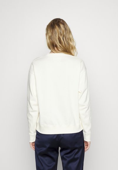 Sweatshirt alb cu decolteu rotund și manșete ribbate. Partea din spate are o textură netedă, combinată cu pantaloni de satin bleumarin.